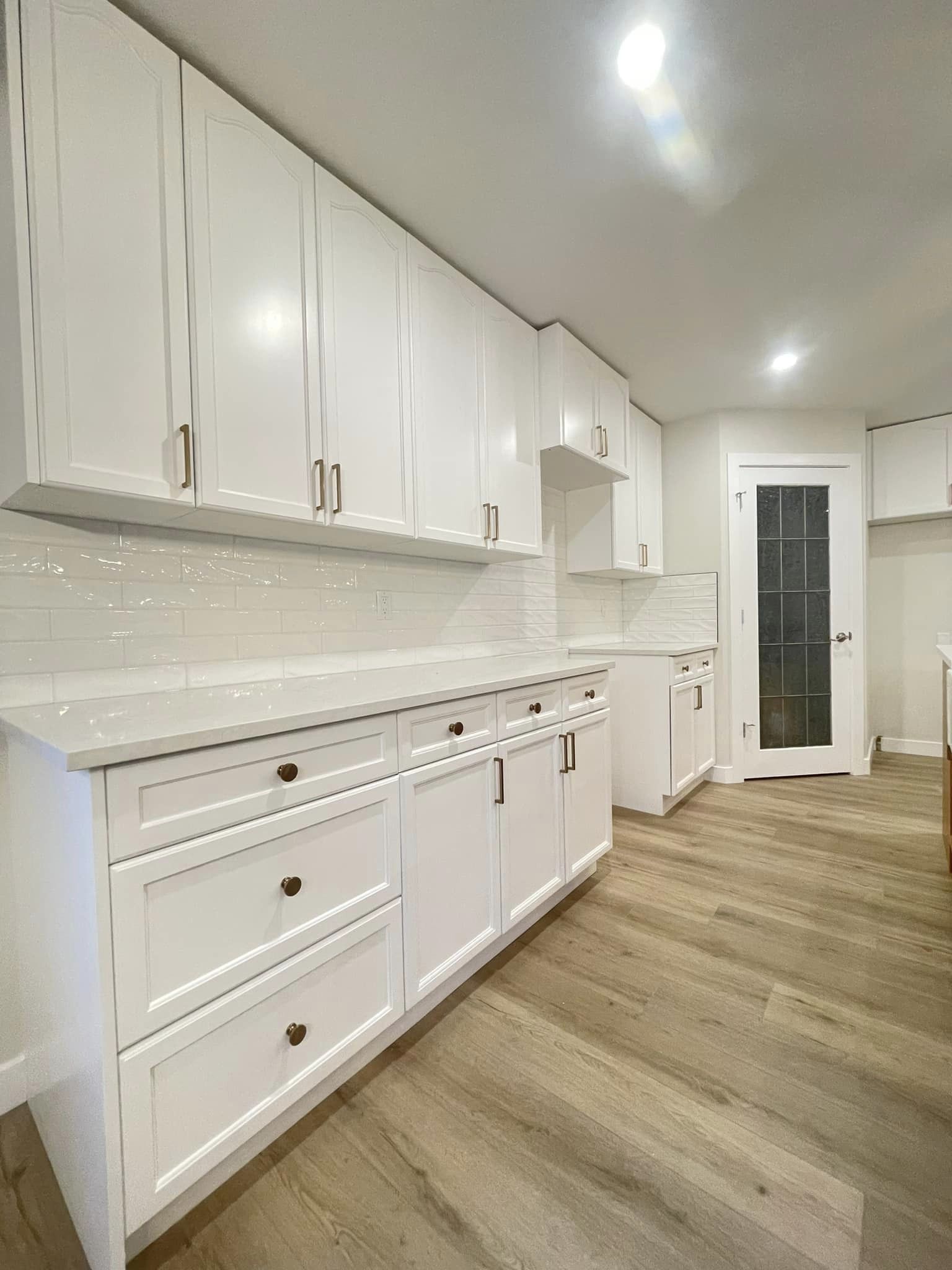 Wide view of a modern kitchen with newly renovated flooring, pantry, counters, and cupboards.