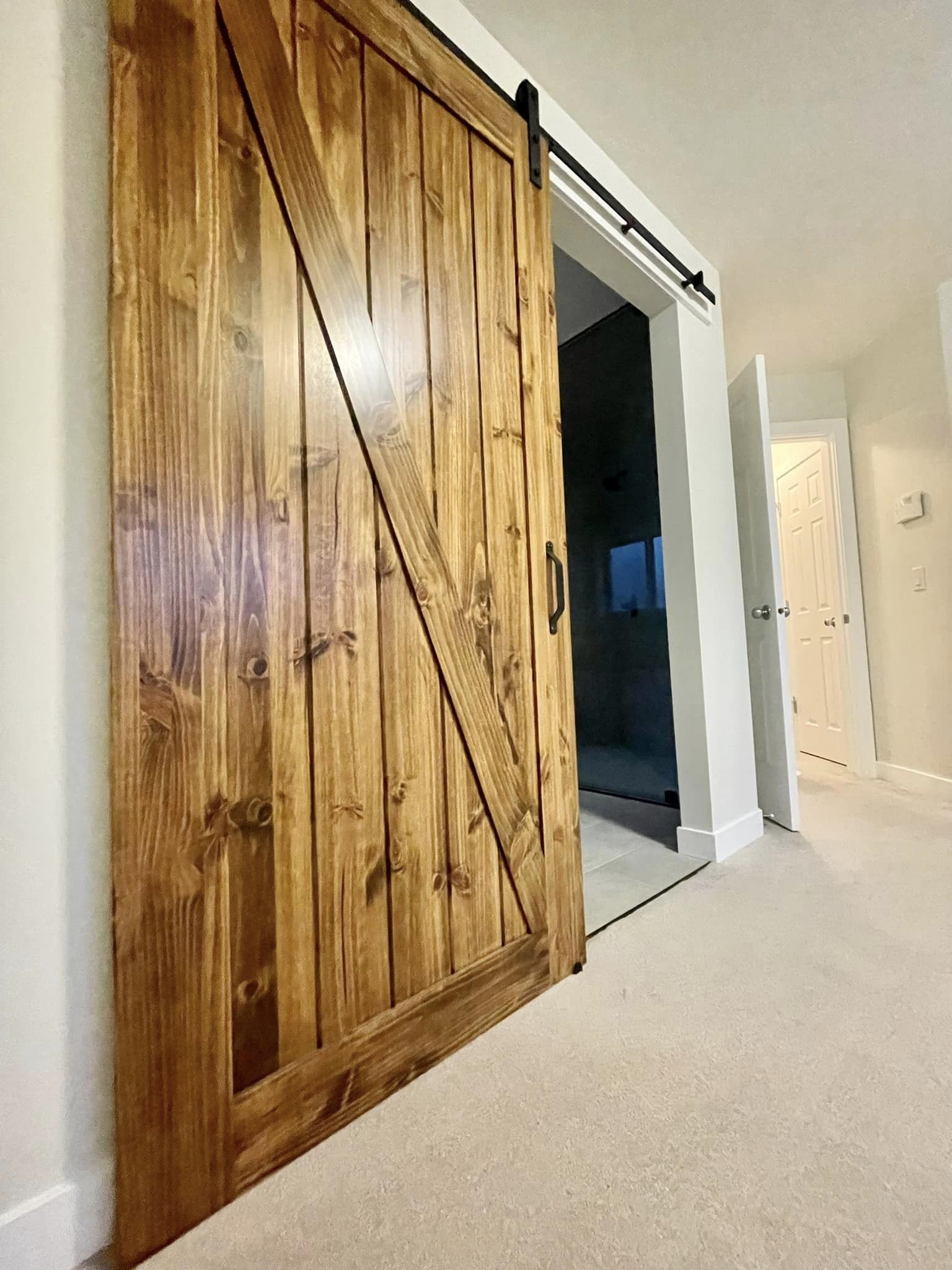 A wide view of the feature wooden barn door entry of a modern bathroom.